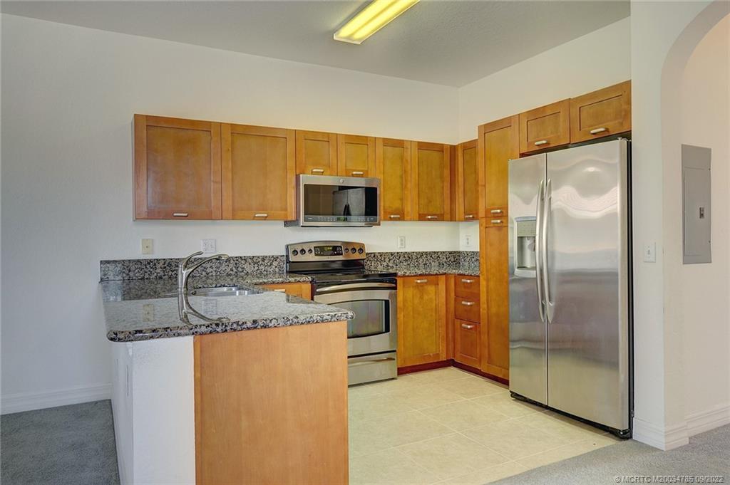 63 Southeast Palermo, Unit 202 Stuart, FL 34994 - Photo 19 of 30 a kitchen with kitchen island granite countertop stainless steel appliances a stove top oven a refrigerator and a sink