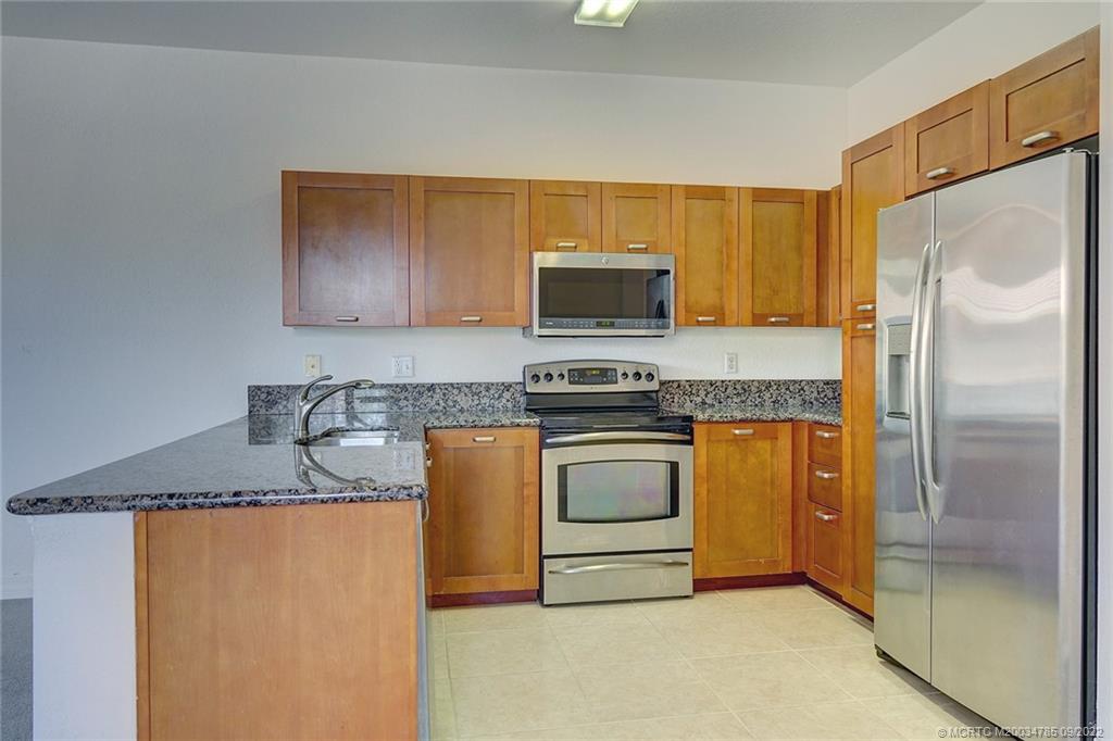 63 Southeast Palermo, Unit 202 Stuart, FL 34994 - Photo 20 of 30 a kitchen with stainless steel appliances granite countertop a refrigerator a stove and a sink with wooden floor