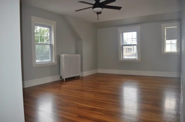 an empty room with wooden floor chandelier fan and windows