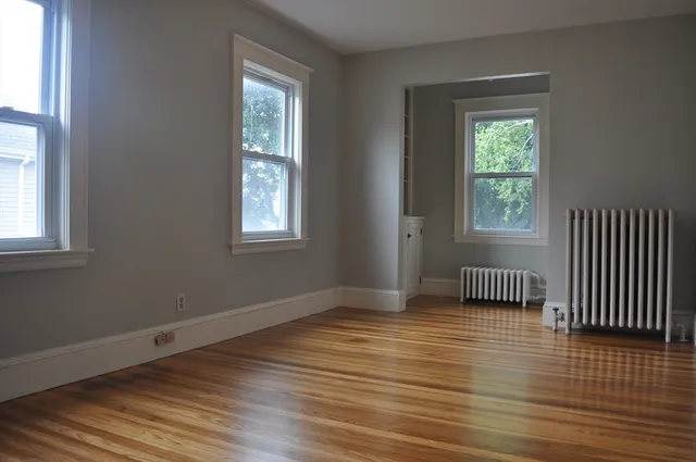 a view of an empty room with wooden floor and a window