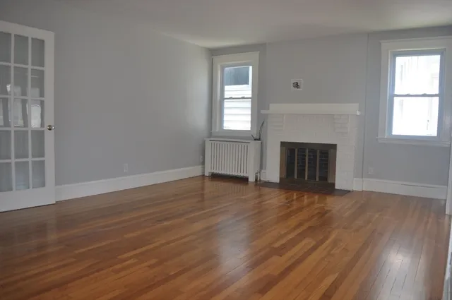 an empty room with wooden floor fireplace and windows