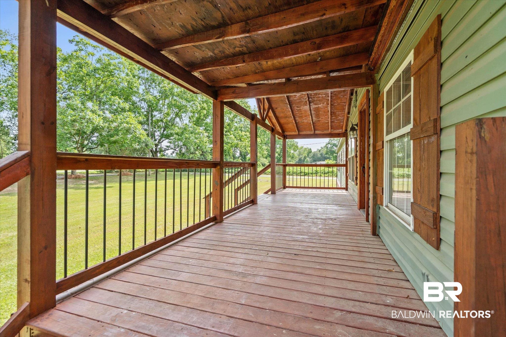 9230 McLeod Road Mobile, AL 36695 - Photo 3 of 20 Expansive covered porch featuring wood-finish flooring, exposed wood beam ceiling, and a wooden railing with black metal spindles