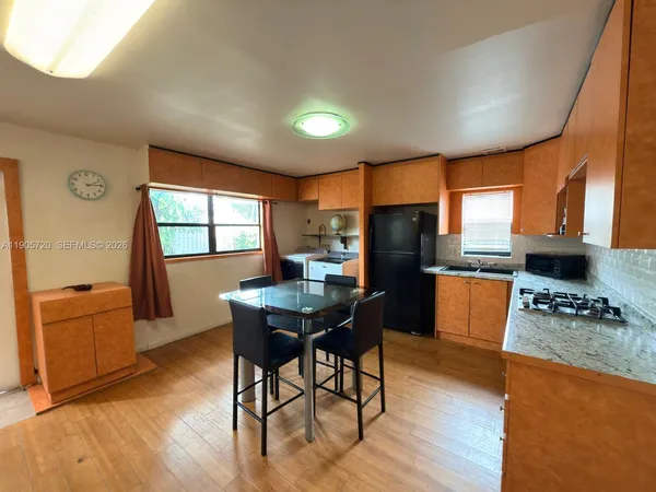 a kitchen with stainless steel appliances granite countertop a stove a refrigerator a sink a dining table and chairs with wooden floor