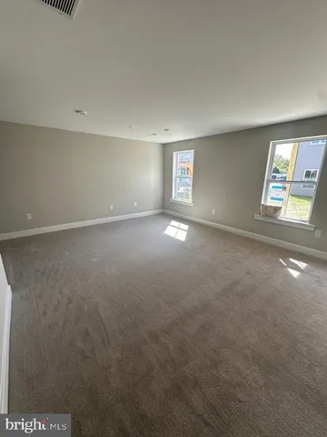 an empty room with windows and view of kitchen