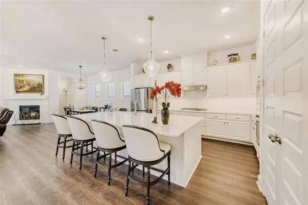 a kitchen with stainless steel appliances a table chairs wooden floors and white cabinets