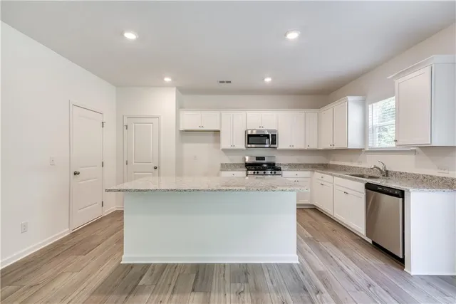 a large kitchen with stainless steel appliances granite countertop a stove a sink and white cabinets