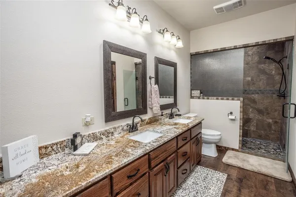 a bathroom with a granite countertop sink a toilet a mirror and shower
