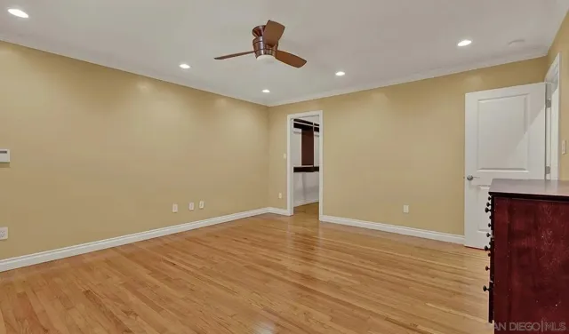a view of an empty room with wooden floor and a ceiling fan