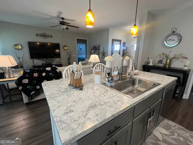 a kitchen with stainless steel appliances granite countertop a sink dishwasher and a flat screen tv with wooden floor