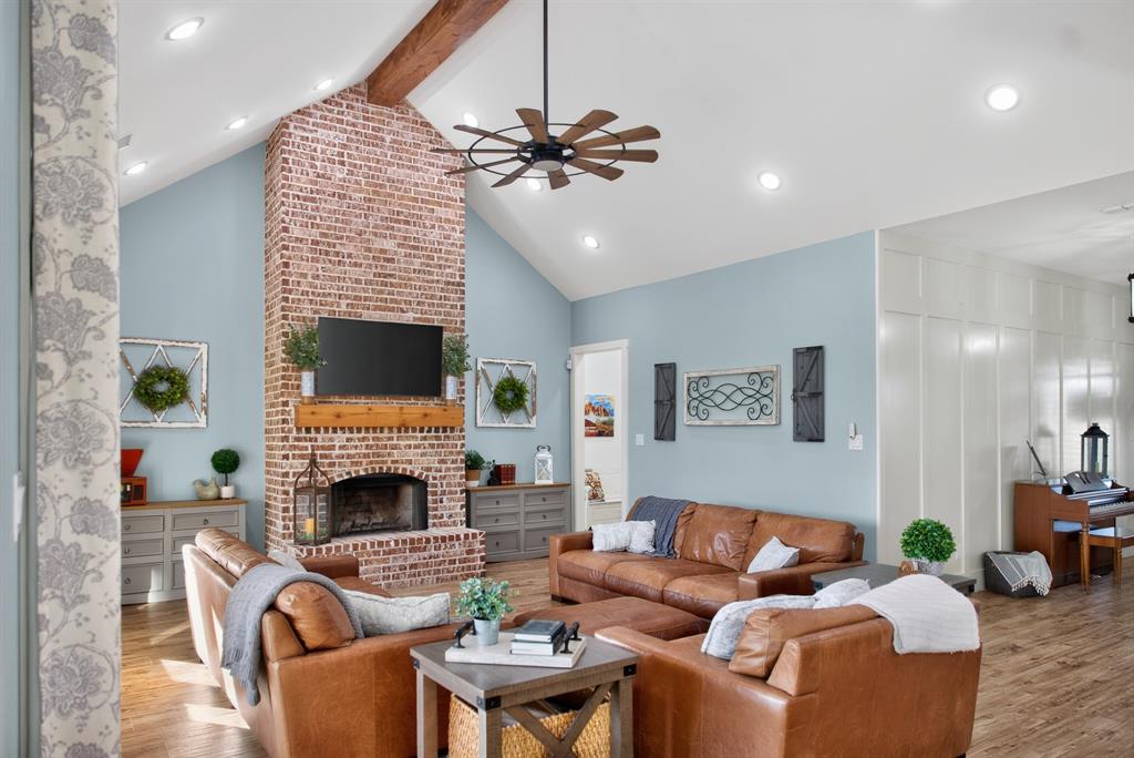 985 Vest Lane Pilot Point, TX 76258 - Photo 22 of 40 Spacious living area featuring a tall brick fireplace with a wood mantle, vaulted ceilings with exposed wood beams, wood-finish flooring, and recessed lighting
