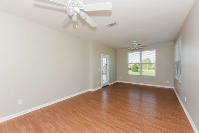 an empty room with wooden floor chandelier fan and windows
