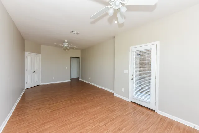 an empty room with wooden floor chandelier fan and windows