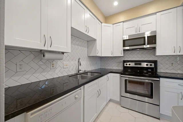 a kitchen with stainless steel appliances granite countertop white cabinets and a stove a sink