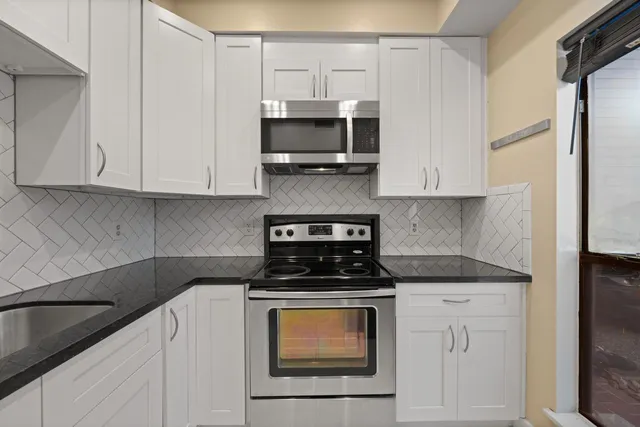 a kitchen with stainless steel appliances granite countertop white cabinets and a stove top oven