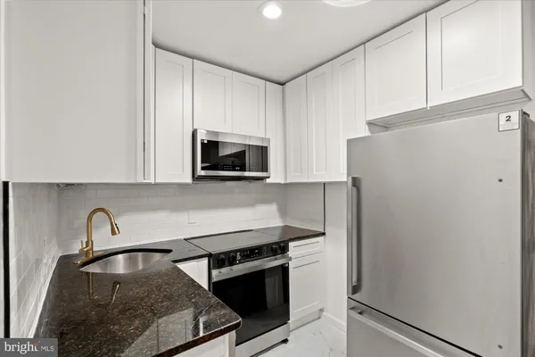 a kitchen with granite countertop a refrigerator stove and white cabinets