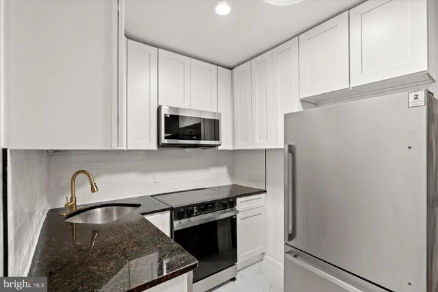 a kitchen with granite countertop a refrigerator stove and white cabinets