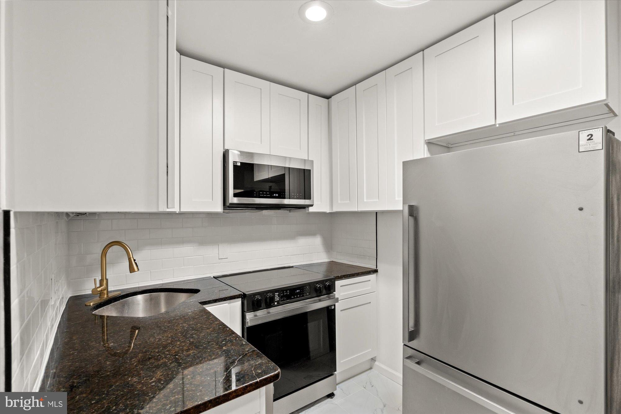 1241 18th Street Northeast, Unit 5 Washington, DC 20002 - Photo 7 of 17 a kitchen with granite countertop a refrigerator stove and white cabinets