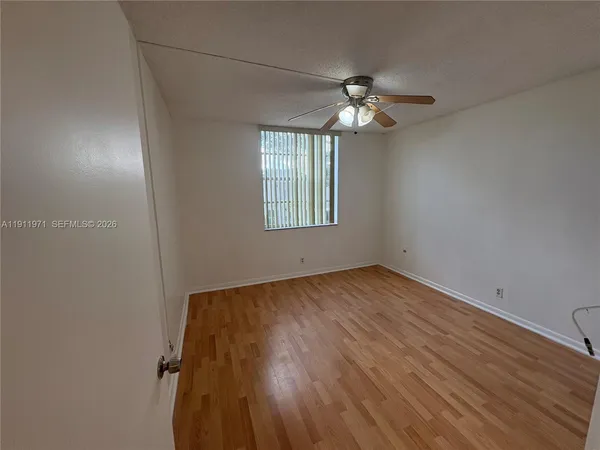 an empty room with wooden floor chandelier fan and windows