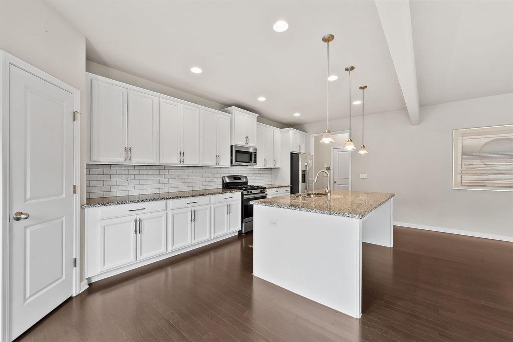 2415 Matlin Way Buford, GA 30519 - Photo 18 of 66 a kitchen with kitchen island a sink a stove a refrigerator and white cabinets with wooden floor