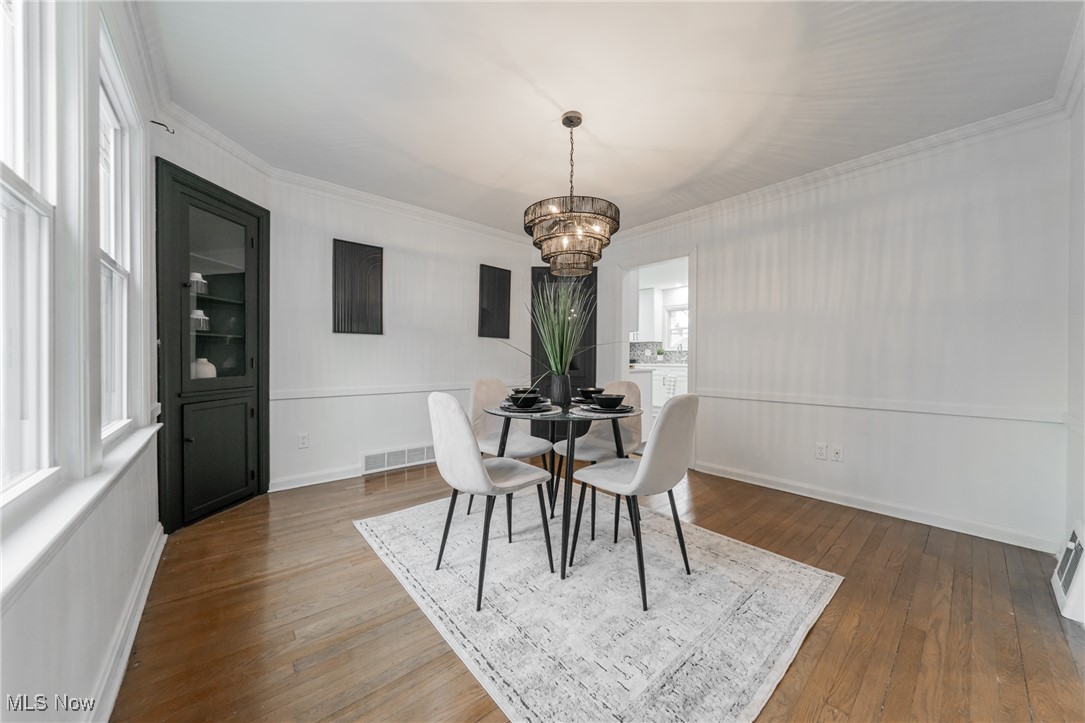 1391 Avondale Road Cleveland, OH 44121 - Photo 12 of 46 Dining area featuring visible vents, baseboards, ornamental molding, hardwood / wood-style floors, and an inviting chandelier