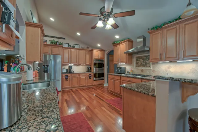 a kitchen with stainless steel appliances granite countertop a refrigerator a sink dishwasher a stove and white cabinets with wooden floor