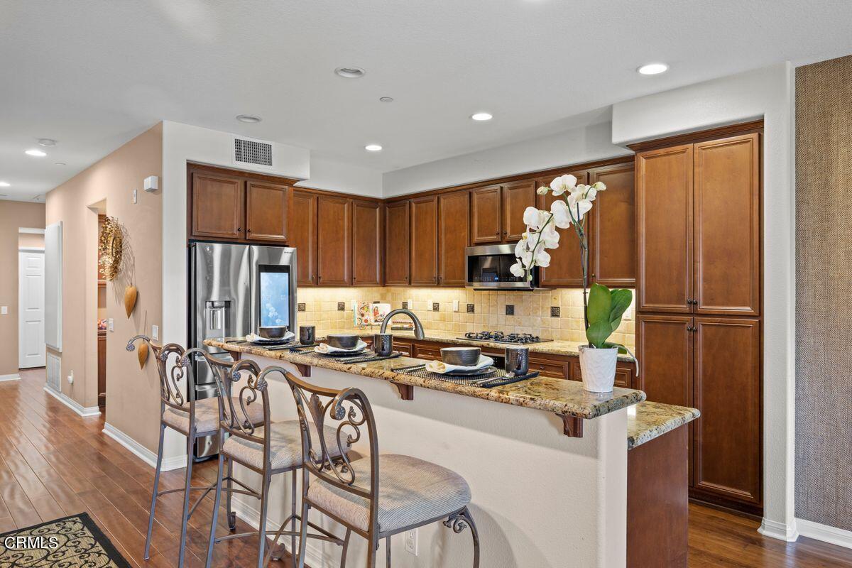 3004 Moonlight Park Avenue Oxnard, CA 93036 - Photo 17 of 28 a kitchen with stainless steel appliances granite countertop a stove a refrigerator a sink a dining table and chairs with wooden floor
