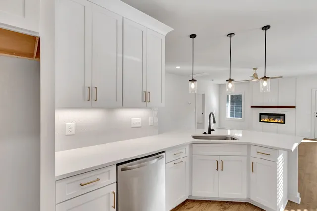 a kitchen with a sink dishwasher and white cabinets with wooden floor