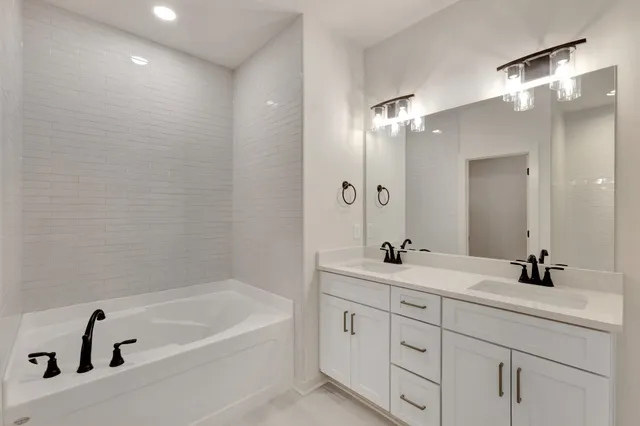 a bathroom with a tub sink double vanity and a mirror