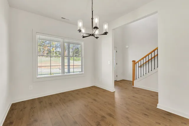 an empty room with wooden floor chandelier fan and windows