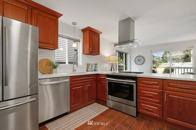 a kitchen with stainless steel appliances granite countertop a refrigerator a stove a sink and white cabinets with wooden floors