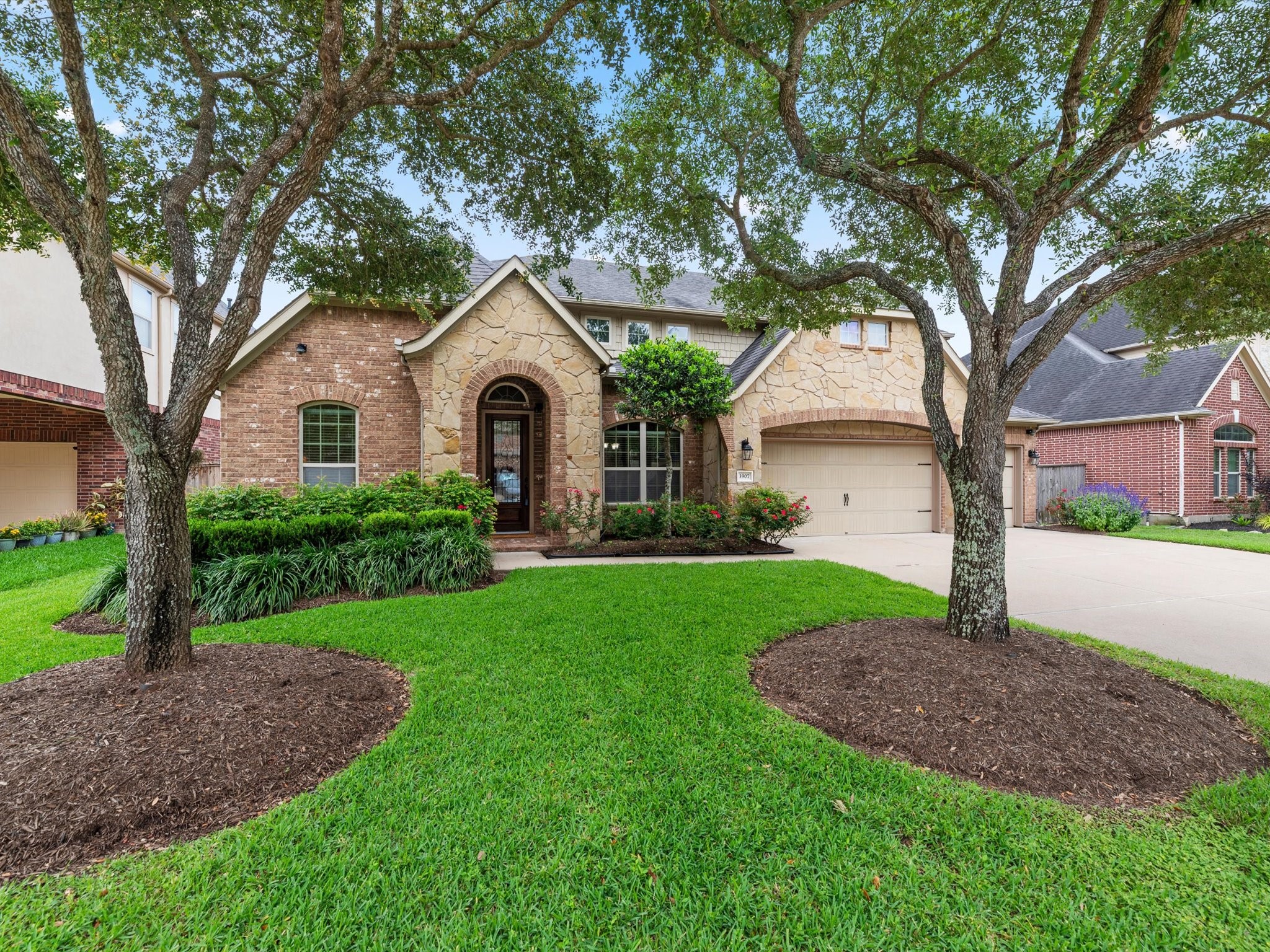 3907 Randle Ridge Court Fulshear, TX 77441 - Photo 43 of 46 This charming home features a blend of stone and brick exterior, with a welcoming arched entryway. The well-manicured front yard includes mature trees and lush landscaping, enhancing its curb appeal. A spacious driveway leads to a three-car garage.