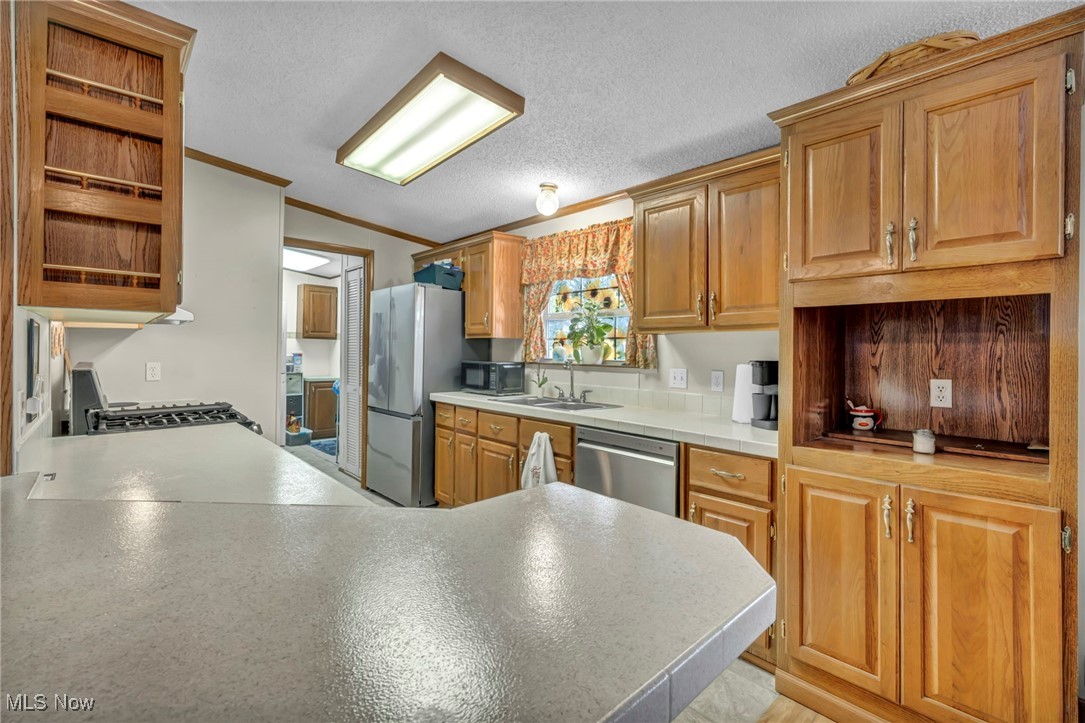 27202 Cook Road, Unit 95 Olmsted Falls, OH 44138 - Photo 16 of 46 Kitchen featuring open shelves, crown molding, light countertops, a peninsula, and stainless steel appliances
