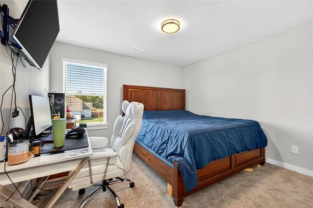 a bedroom with a bed a computer on the desk and a dresser next to a window