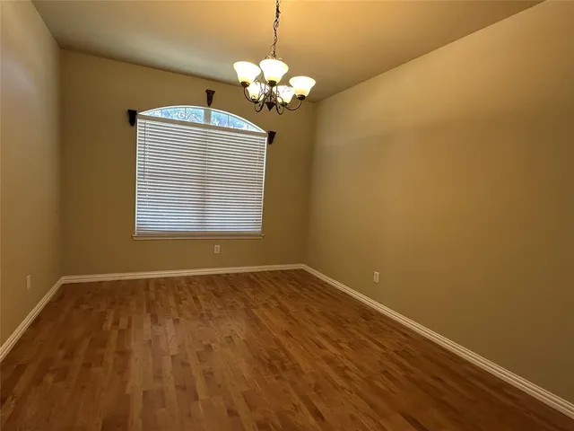 a view of an empty room with chandelier and wooden floor