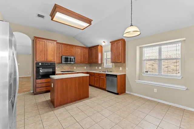 a large kitchen with stainless steel appliances granite countertop a refrigerator a sink dishwasher a stove with wooden cabinets and a dining table