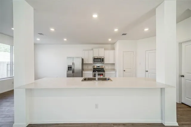 a kitchen with stainless steel appliances a refrigerator a sink a stove top oven a wooden floor and cabinets