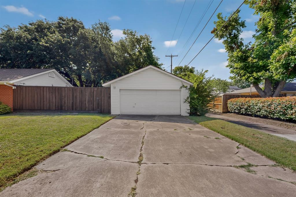Detached white siding garage with a single garage door, concrete driveway, and surrounding green lawn