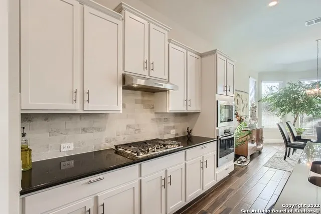 a kitchen with granite countertop a sink a stove and white cabinets