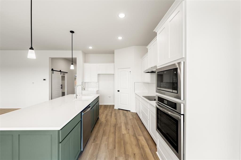 125 Snowy Owl Trail Rhome, TX 76078 - Photo 11 of 28 Dual tone kitchen featuring two tone color scheme, a barn door, stainless steel appliances, a kitchen island with sink, and light wood-style floors
