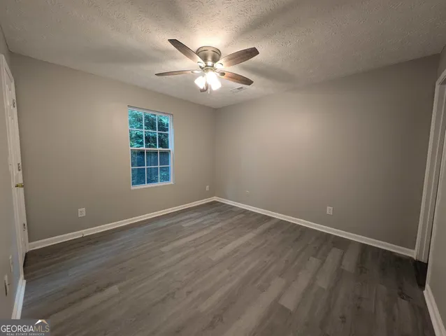 an empty room with wooden floor fan and windows