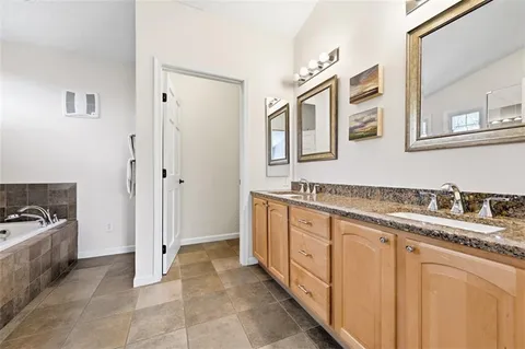 a spacious bathroom with a granite countertop sink a mirror a bathtub and next to a window