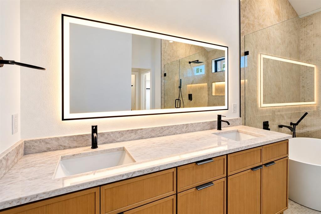 1640 West Wintergreen Road Lancaster, TX 75134 - Photo 23 of 37 Dual vanity with integrated sinks, light-toned stone countertop, wood-finish cabinetry with dark hardware, back-lit mirror, and matte black fixtures