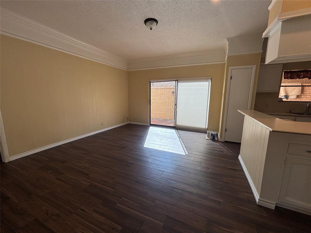 4702 Ranch View Road Fort Worth, TX 76109 - Photo 11 of 40 Wood-finish flooring, crown molding, sliding glass door, white kitchen cabinetry, and a kitchen island with a light-toned countertop