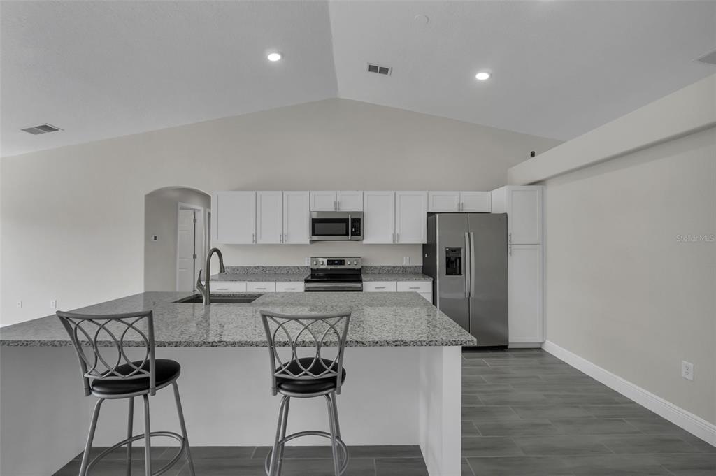 506 Peace Way Kissimmee, FL 34759 - Photo 9 of 34 a kitchen with stainless steel appliances granite countertop a sink a stove a refrigerator a microwave oven with white cabinets and wooden floor
