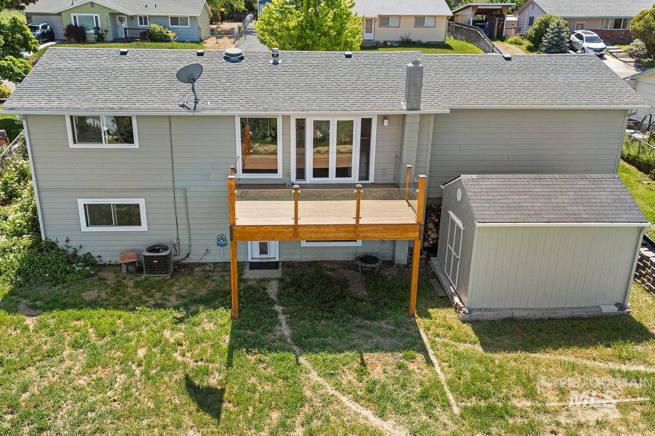 10178 West Fox Ridge Drive Boise, ID 83709 - Photo 28 of 36 Rear exterior featuring a wooden deck with glass panel railings, grey siding, and a detached shed with a shingle roof
