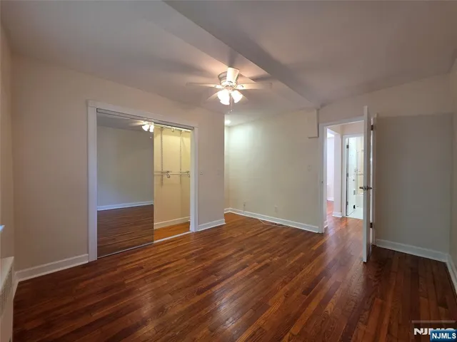 a view of an empty room with wooden floor and a kitchen