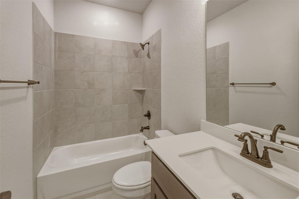 1213 Colca Drive Springtown, TX 76082 - Photo 14 of 23 Bathroom featuring a white tub, light-toned tile surround, bronze-finish fixtures, and a vanity with an integrated sink and white countertop