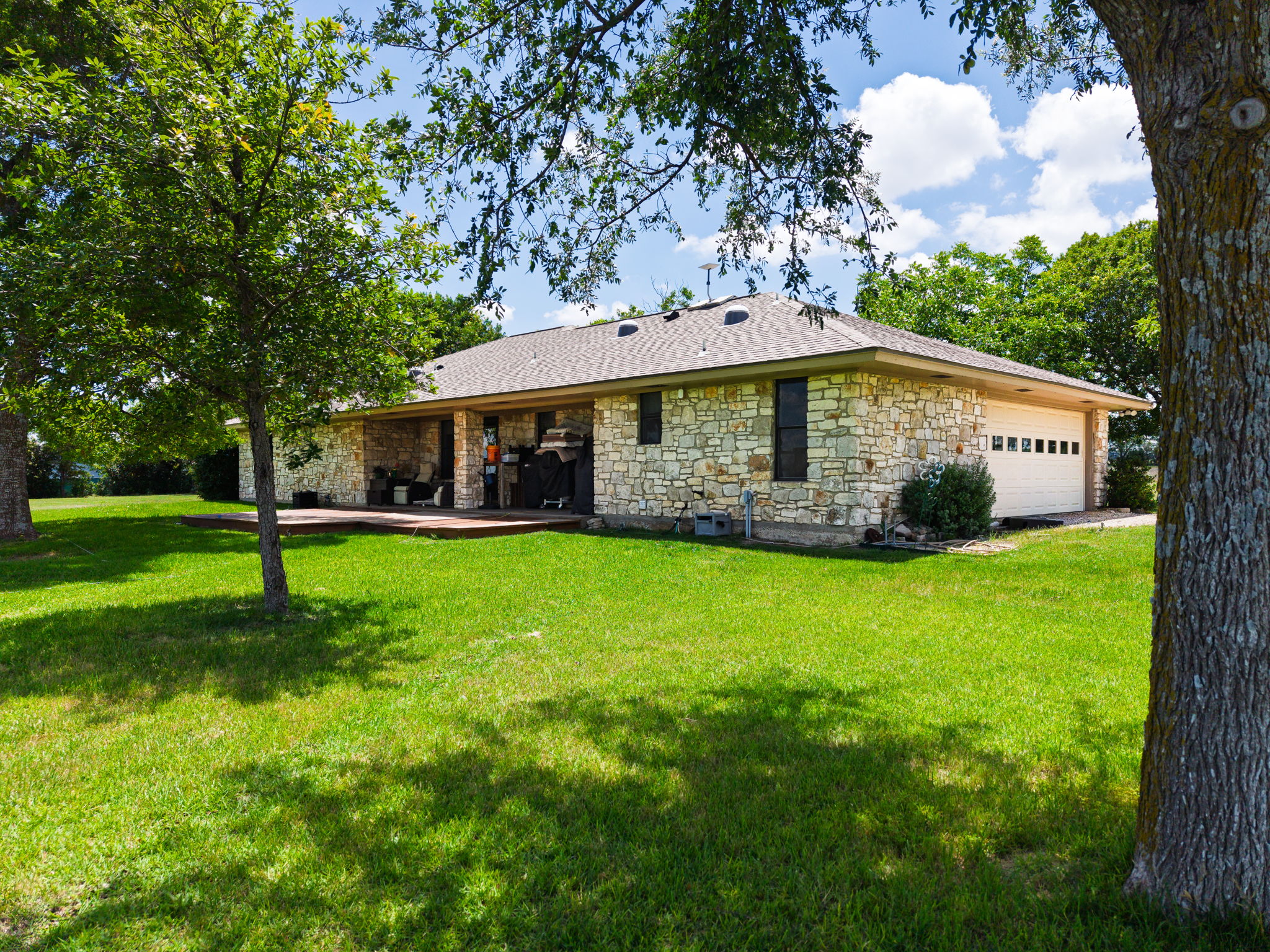 120 Rae Lane Jarrell, TX 76537 - Photo 26 of 40 Stone veneer exterior with a covered patio, a two-car garage with panel windows, and a shingle roof