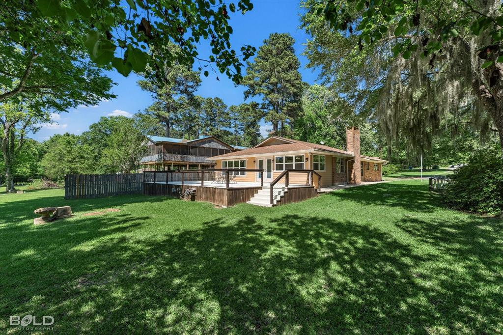 225 Marie Road Ringgold, LA 71068 - Photo 13 of 40 Expansive backyard featuring a large wood deck with white railings, a brick chimney, and mature trees providing natural shade