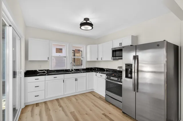a kitchen with granite countertop a refrigerator a sink and white cabinets